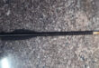 A black dart with a metal tip laying on a speckled gray stone surface. The dart is horizontally positioned, with minimal shadows.
