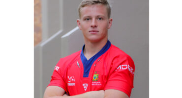 Young man in a red sports jersey, arms crossed, standing confidently against a gray urban backdrop. The tone is serious and determined.