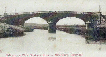 Vintage postcard of an arched stone bridge over Klein Olifants River in Middelburg, Transvaal. The bridge reflects into the calm water below.