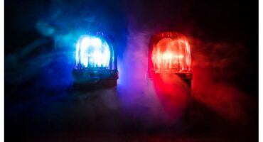 Two police siren lights, blue on the left and red on the right, illuminated amid swirling mist in a dark setting, creating a dramatic, urgent atmosphere.