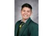 Smiling young person in a formal green school uniform with a tie, against a gray backdrop. The expression conveys warmth and confidence.