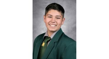 Smiling young person in a formal green school uniform with a tie, against a gray backdrop. The expression conveys warmth and confidence.