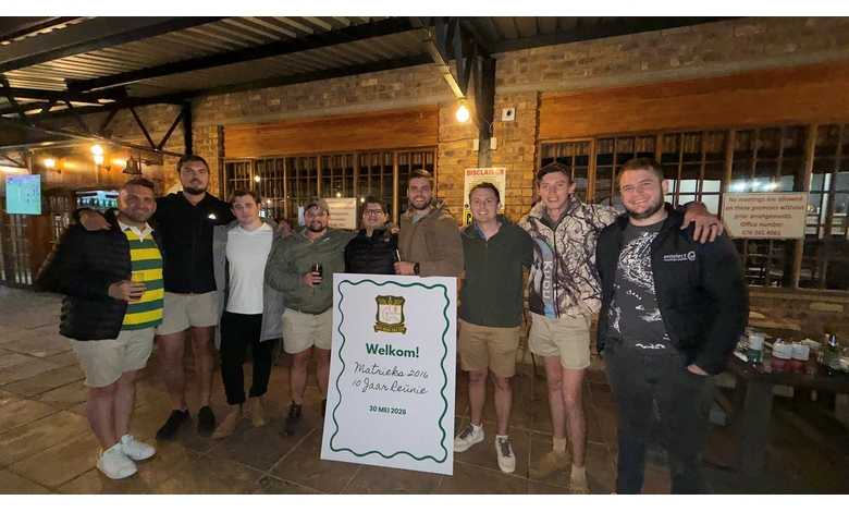 A group of nine people stand closely together, smiling at the camera. They are dressed casually, with a sign in front welcoming a 2016 alumni reunion on May 30, 2026. The setting is a rustic indoor space with brick walls and warm lighting, creating a friendly and celebratory atmosphere.