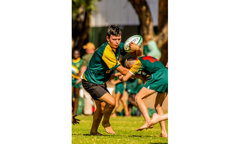 Two young rugby players in green jerseys are engaged in a match on a sunny day. One player is holding a rugby ball, evoking determination and focus.