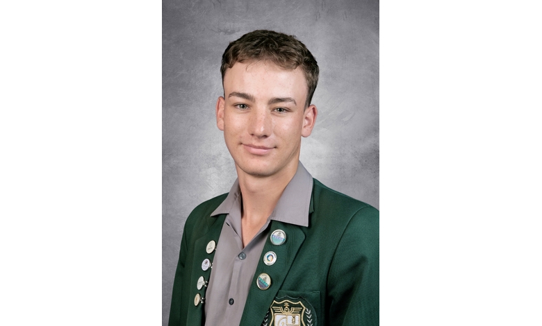 Young man in a green blazer with school badges poses confidently against a gray backdrop, conveying a sense of pride and achievement.