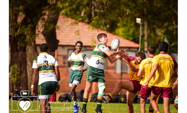 Young athletes play rugby in a park. A player in green and white jumps to catch the ball, while opponents in red and yellow try to block, showing intensity.