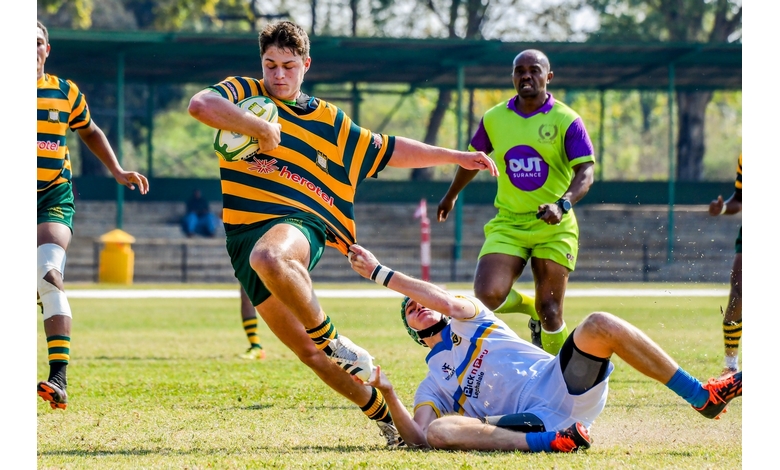 A rugby player in green and yellow stripes evades a tackle from a player in white. The referee, in bright green, observes. The scene conveys action and intensity.
