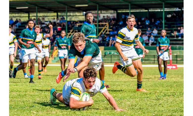 A rugby player in a white and green uniform scores a try, passionately chased by opponents in green jerseys. Teammates and spectators cheer in the background.