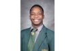 Smiling young man in a green school blazer and tie against a gray background, projecting confidence and positivity.