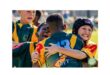 Young rugby players in colorful jerseys embrace joyfully on the field, expressing excitement and camaraderie. The sunlight hints at a warm day.
