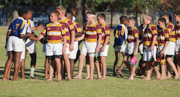 A group of young rugby players in striped jerseys and white shorts shake hands after a match on a grassy field, conveying sportsmanship and camaraderie.