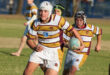 A youth rugby player in a yellow and maroon striped jersey runs with a ball, focused and determined, while teammates follow on a grassy field.