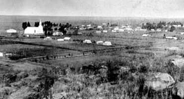 Black and white photo of a rural 1800s village. A prominent church is surrounded by fields and scattered houses, creating a serene, historical atmosphere.