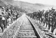 A group of soldiers in uniform standing on railroad tracks, looking serious and attentive to their surroundings.