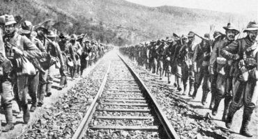 A group of soldiers in uniform standing on railroad tracks, looking serious and attentive to their surroundings.