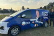 A man stands beside a blue campaign van on grass. The van displays a large image of another man with text "Bosman Grobler for Mayor" and "DA."