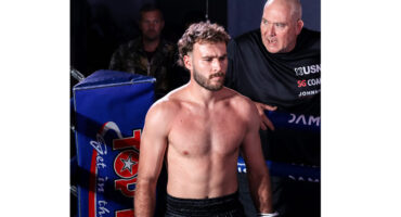 A muscular, shirtless man poses in a boxing ring, showcasing his physique and preparing for an upcoming fight.