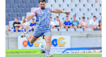 A rugby player in action, preparing to kick the ball on a grassy field during a match.