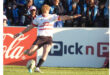 A rugby player in action, kicking a ball high into the air during a match.