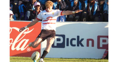 A rugby player in action, kicking a ball high into the air during a match.