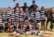 A diverse group of young boys and girls wearing rugby uniforms, smiling and posing together on a field.