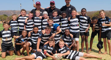 A diverse group of young boys and girls wearing rugby uniforms, smiling and posing together on a field.