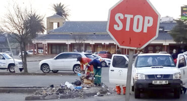 A stop sign alongside a man and woman in work attire, actively performing maintenance tasks on the roadside.