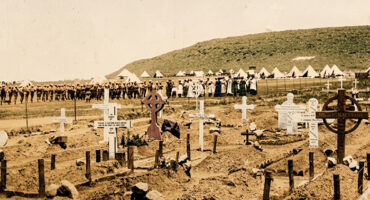 Rows of white and wooden crosses mark graves in a barren cemetery. Soldiers and people line up in the background by white tents, conveying a somber tone.