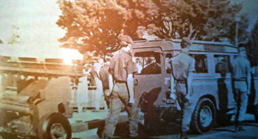 A group of soldiers gathered around a truck, engaged in conversation and examining its features.