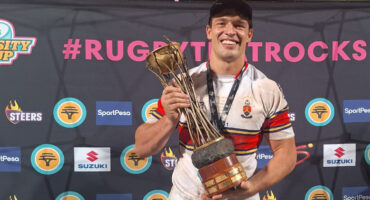 A man proudly holds a trophy in front of a decorative wall, showcasing his achievement.