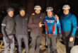 A group of men in cycling gear smiling and posing together for a photo outdoors