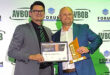 Two men proudly display an award in front of a decorative wall.