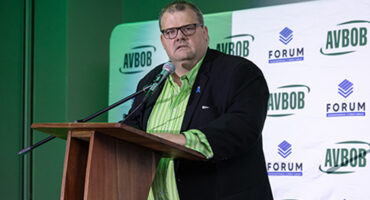 A man wearing glasses delivers a speech at a podium, engaging the audience with his presentation.