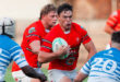 Rugby players in red and white jerseys compete on the field during an intense match.