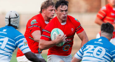 Rugby players in red and white jerseys compete on the field during an intense match.