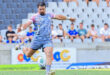 A rugby player in action, preparing to kick the ball on a grassy field during a match.