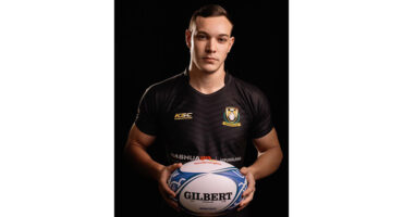 A man wearing a black shirt stands holding a ball, looking focused and ready for action.