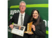 A man and woman celebrate with an award, positioned in front of a bright green wall.