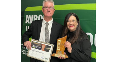 A man and woman celebrate with an award, positioned in front of a bright green wall.