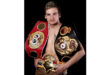 A man proudly displays multiple boxing belts draped across his chest, showcasing his achievements in the sport.