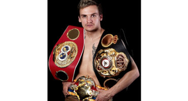A man proudly displays multiple boxing belts draped across his chest, showcasing his achievements in the sport.