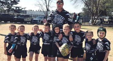A group of young boys wearing black and white jerseys, standing together in a rugby setting.