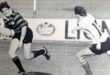 Black and white photo of two men engaged in a rugby match, showcasing athleticism and teamwork on the field.