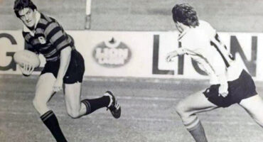 Black and white photo of two men engaged in a rugby match, showcasing athleticism and teamwork on the field.
