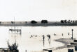 Black and white photo of a dam with several people swimming and enjoying the water on a sunny day.