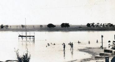 Black and white photo of a dam with several people swimming and enjoying the water on a sunny day.