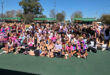 A group of girls smiling and posing together on a netball court, with netball equipment visible in the background.