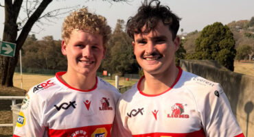 Two young men wearing red and white jerseys stand side by side, smiling at the camera.