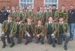 A group of boys wearing green and yellow jackets, standing together outdoors, smiling and engaging with each other.