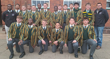 A group of boys wearing green and yellow jackets, standing together outdoors, smiling and engaging with each other.